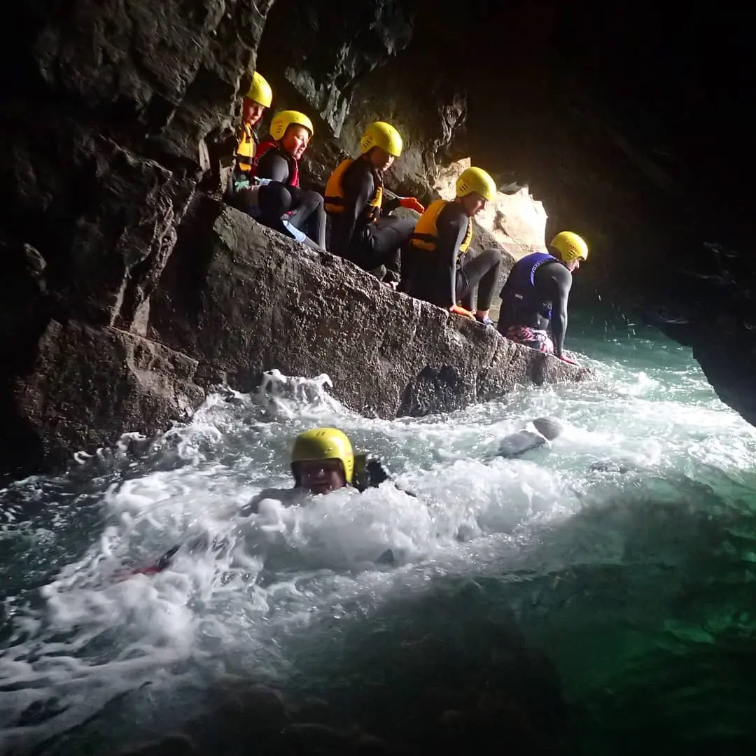 Coasteering group swimming through a sea cave in Pembrokeshire